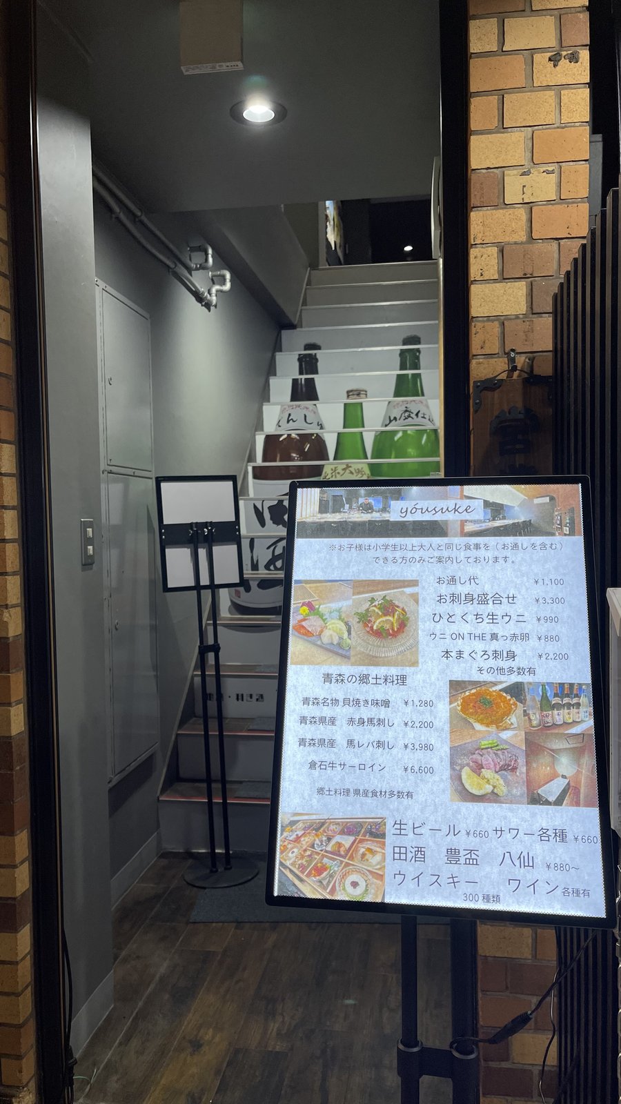 ビルの階段に日本酒の瓶が並ぶ、居酒屋「yousuke」の入り口とメニュー看板